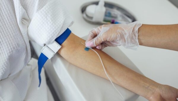 Young brunette woman in a white coat makes medical procedures. A nurse in gloves and medical clothes takes blood or puts a dropper on the patient. Medical services and health concept. Copy space